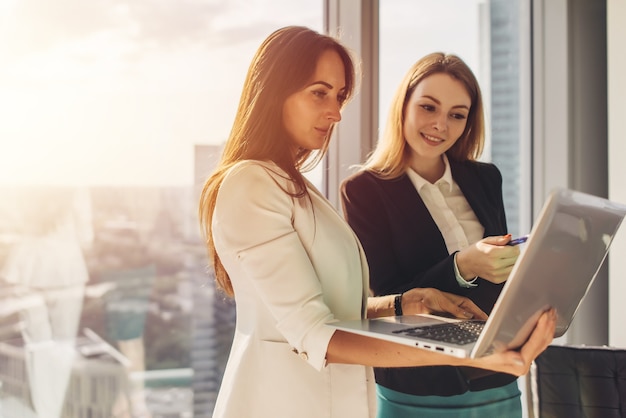 Smiling smart coworkers holding a laptop discussing new ideas standing in office.