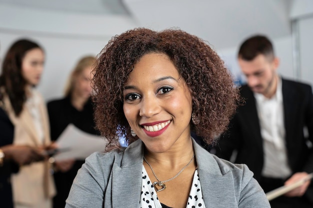 Smiling south american business woman working inside modern office with the multiethnic team behind her Concept of leadership and achieving goals Focus on eyes