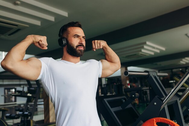 ジムで彼の筋肉を示す白い t シャツで笑顔のスポーツ男