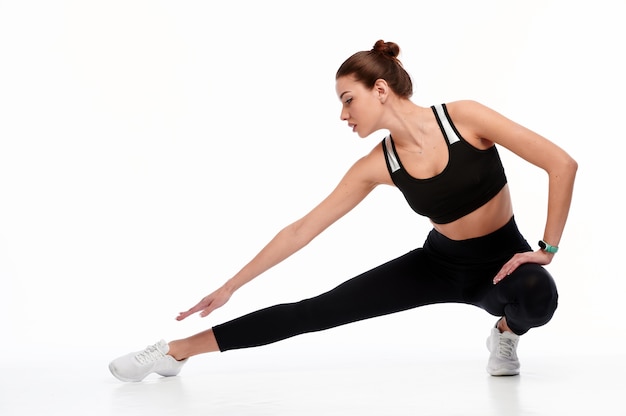 Smiling sports woman stretching legs while isolated on a white background