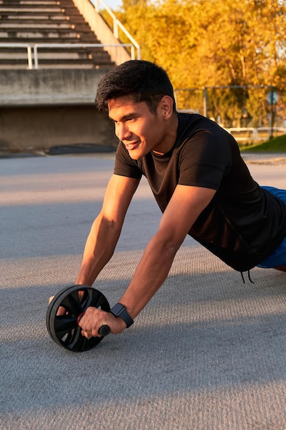 Smiling sportsman training with an abdominal roller Vertically