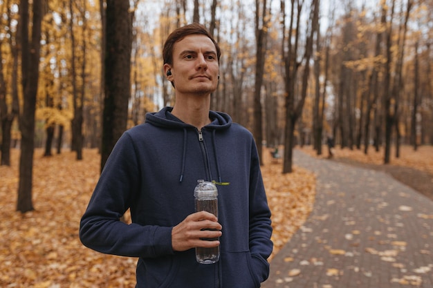 秋の公園でのトレーニング中に休憩を取って水のボトルを持つ笑顔のスポーツマン