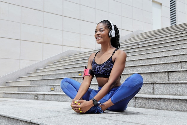 Smiling sportswoman doing butterfly exercise to strech her legs after morning run