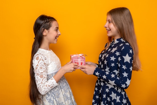 Smiling standing in profile view two little girls holding present