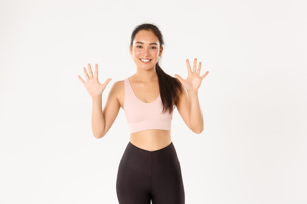 Smiling strong and slim asian female fitness instructor teaching lesson, white background.