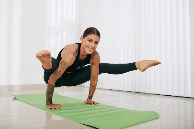 Smiling strong young woman standing on hands, raising legs and looking at camera