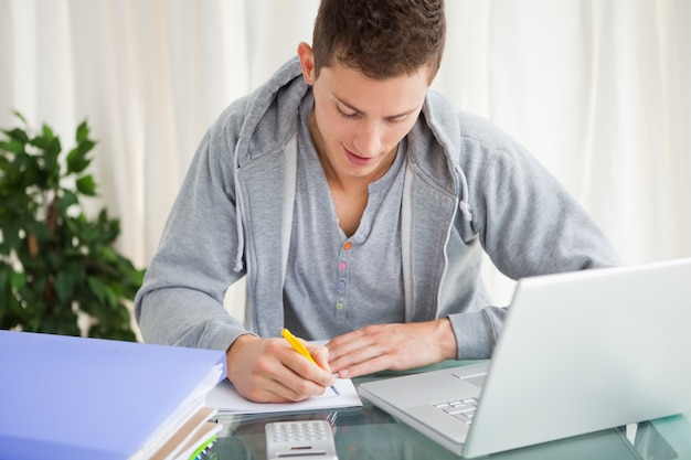 Photo smiling student doing his homework with a laptop