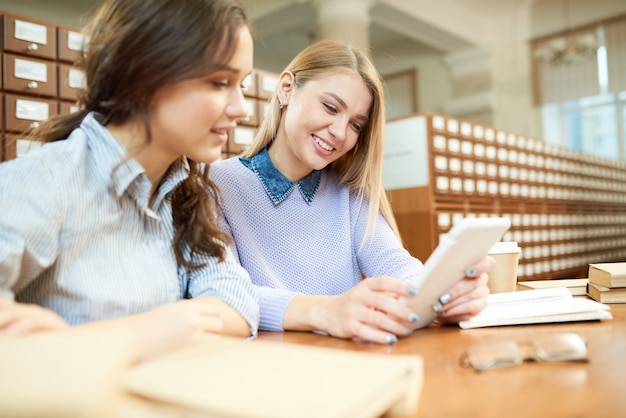 Smiling student friends reading online article in library