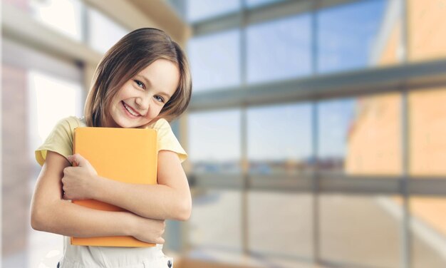 学校のバックパックを身に着けて、練習帳を持っている笑顔の学生の女の子。