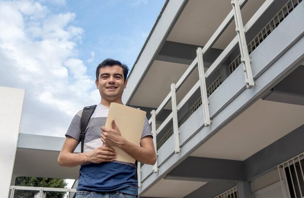 Foto studente sorridente con un giornale in mano davanti a un edificio scolastico