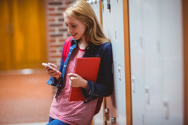 スマートフォンを使ってロッカーに傾いている笑顔の学生