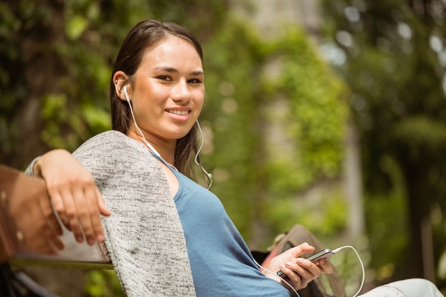 Foto studente sorridente che si siede sulla musica d'ascolto del banco con il telefono cellulare