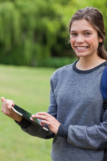 Smiling student using her tablet pc while standing in a park