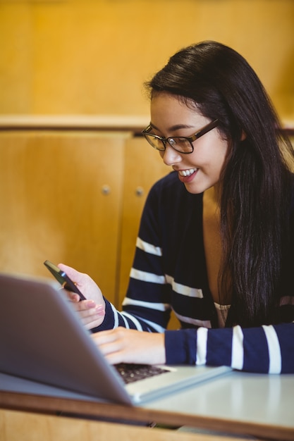 Smiling student using laptop and smartphone during class