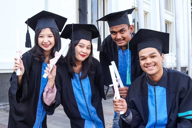 Smiling students in academic caps and gowns celebrating graduation holding certificates and looking