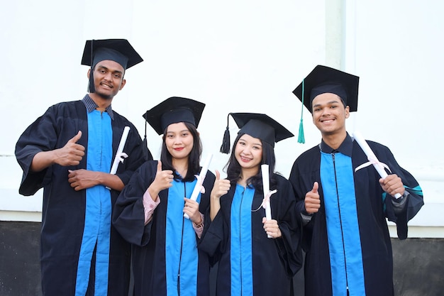 Smiling students in academic caps and gowns celebrating graduation holding certificates and showing