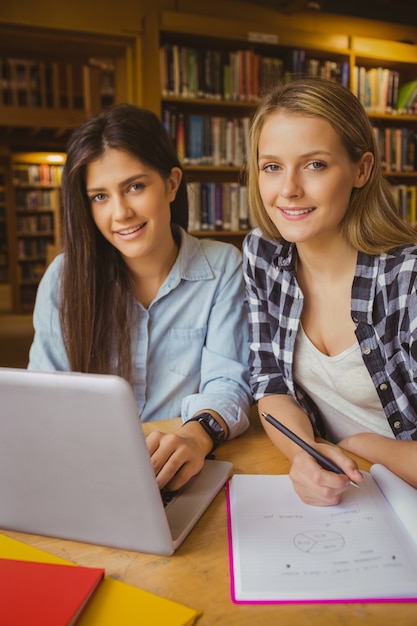 Smiling students using laptop in library 