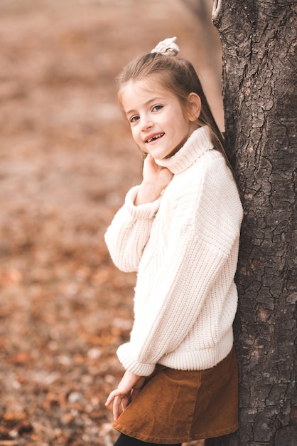 Smiling stylish child girl wear knit sweater with yellow leaves over nature background outdoors