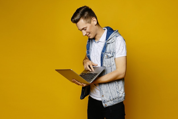 Foto tipo alla moda sorridente in attrezzatura casuale che posa con il computer portatile su fondo giallo arancione, isolato. giovane uomo bello con il taccuino nelle mani.