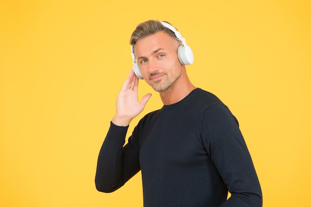 Smiling stylish mature guy with trendy hairstyle wearing earphones listening ebook or audio book for study online, digital technology.