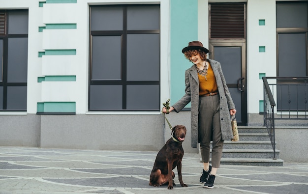 Улыбающаяся стильная женщина и коричневая собака на поводке