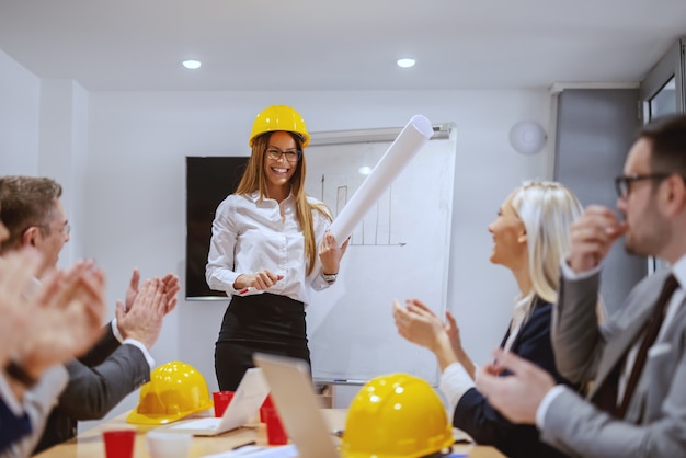 Foto riuscito architetto femminile sorridente che sta alla sala del consiglio e che parla del nuovo progetto. colleghe che le applaudono. se fai ciò che hai sempre fatto, otterrai ciò che hai sempre ottenuto.