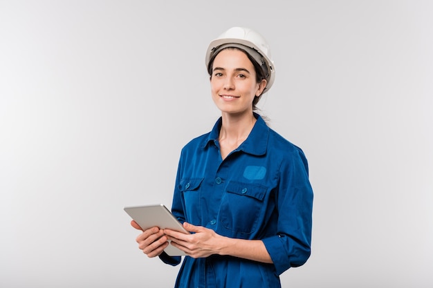 Sorridente ingegnere femminile di successo in abiti da lavoro e elmetto protettivo utilizzando il touchpad durante il collegamento in rete in isolamento