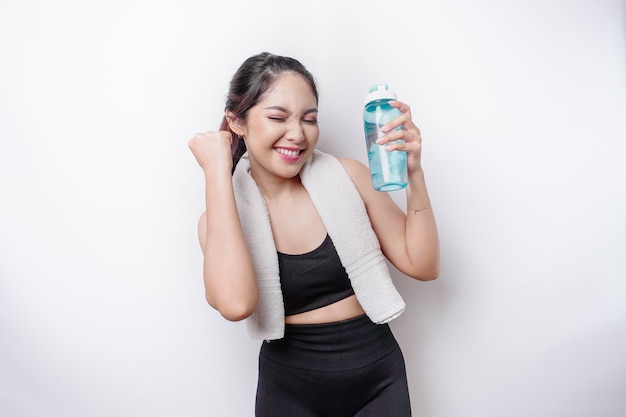 Smiling successful sportive Asian woman posing with a towel on her shoulder and holding a bottle of water