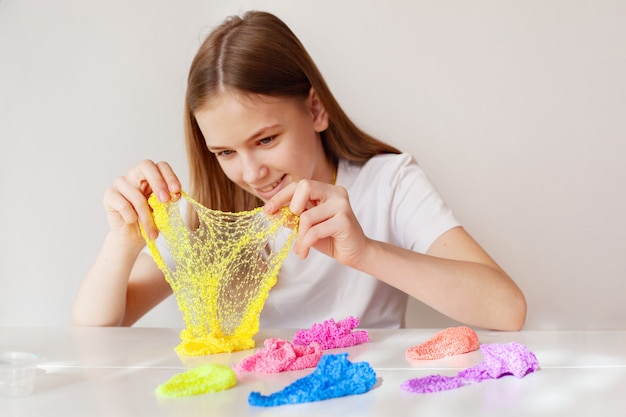 A smiling sweet girl looks at the yellow slime and stretches it to transparency