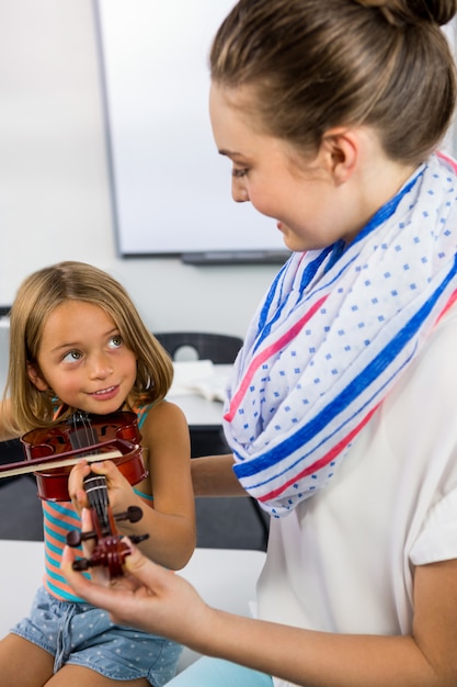 Smiling teacher assisting girl to play violin in classroom