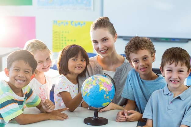 Smiling teacher and schoolchildren with globe on table