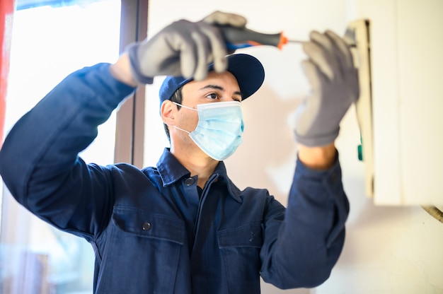 코로나바이러스 전염병으로 인해 마스크를 쓰고 온수 히터를 수리하는 웃는 기술자