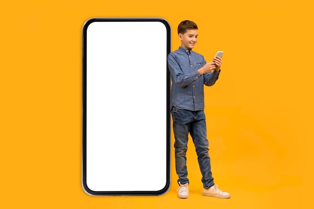 Smiling teen boy using cellphone while standing next to blank smartphone screen