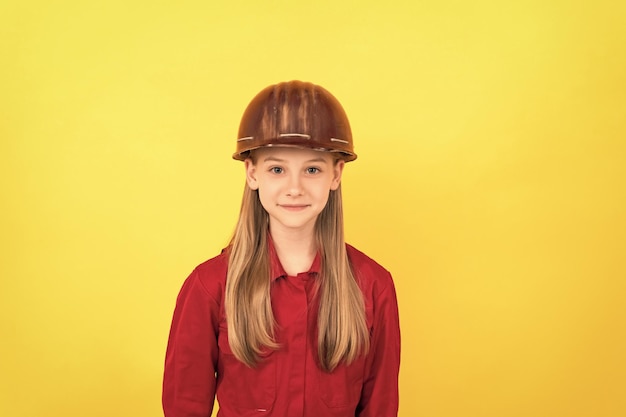 Smiling teen child in builder helmet on yellow background