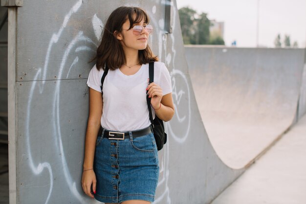 Smiling teen girl in glasses and braces while standing alone against a wall on a street.