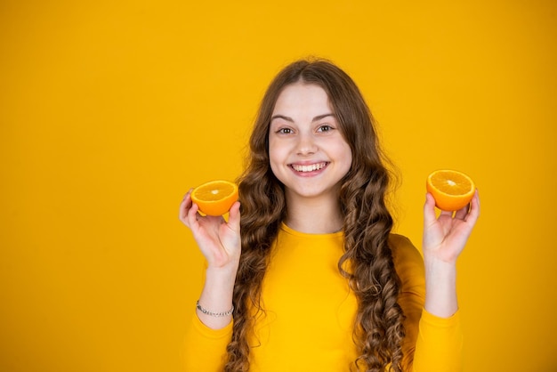 Smiling teen girl hold orange fruit on yellow background
