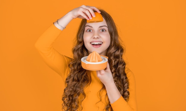 Smiling teen girl hold orange and juicer on yellow background