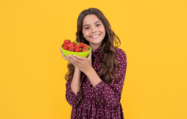 Smiling teen girl hold strawberry bowl on yellow background