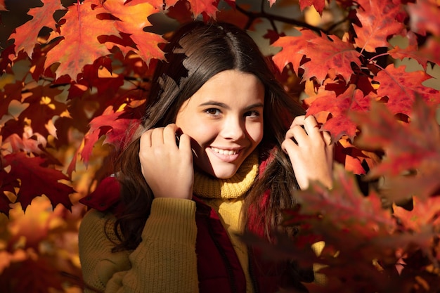 Smiling teen girl standing at beautiful autumn leaves