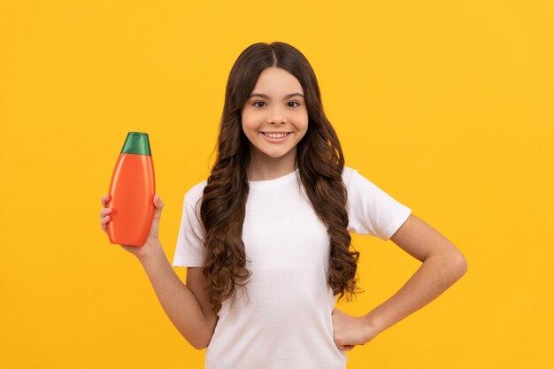 Smiling teen girl with long hair hold shampoo bottle promotion