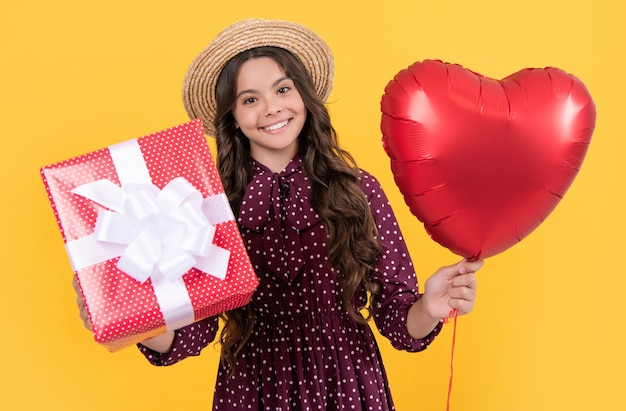 Smiling teen girl with red heart balloon and present box on yellow background