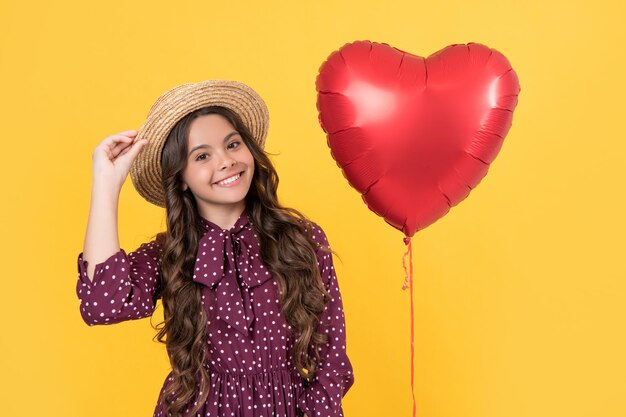 Улыбающаяся девочка-подросток с красным сердечным шаром на желтом фоне