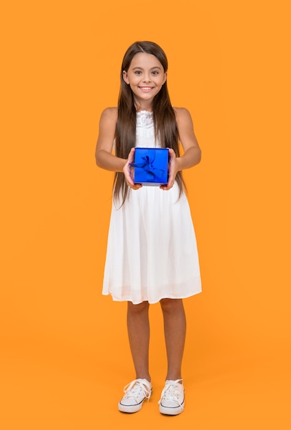 Smiling teen kid hold present box on yellow background