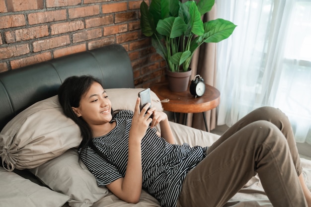 Ragazza asiatica adolescente sorridente che per mezzo dello smartphone