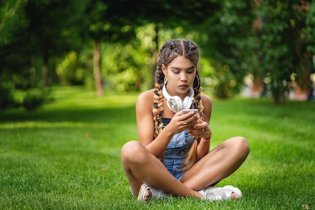 Smiling teenage black girl using a phone sitting on the grass