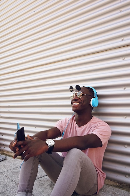 Photo smiling teenage boy listening music while sitting against wall