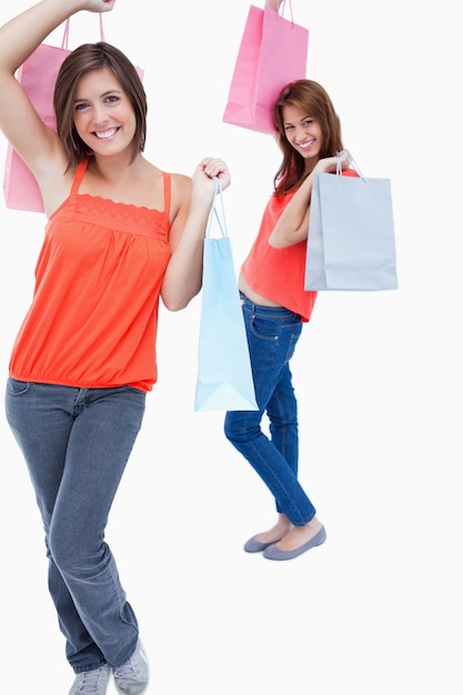 Smiling teenage girl followed by a friend and both are holding purchase bags