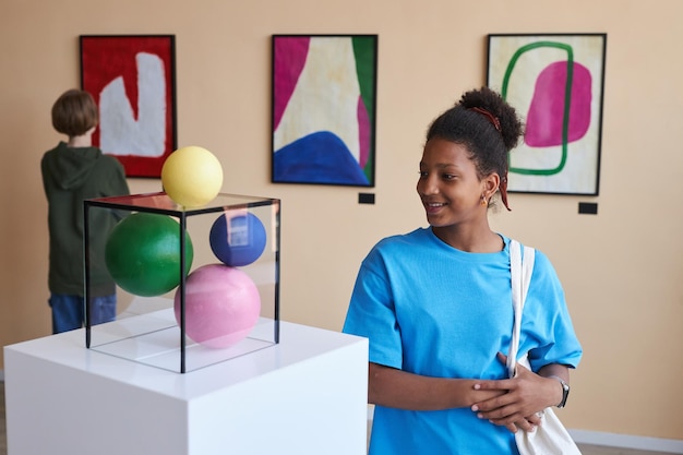 Smiling teenage girl looking at abtract sculpture in museum