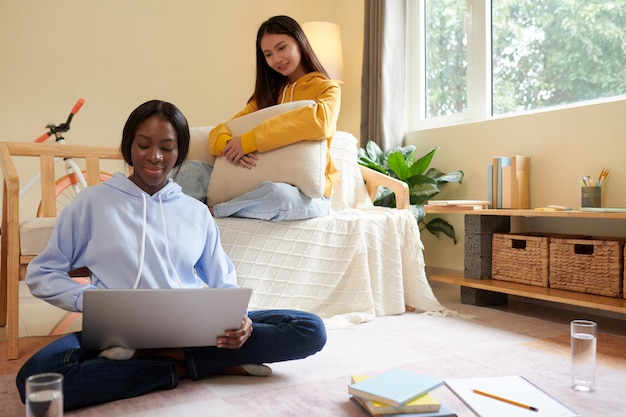 Photo smiling teenage girl looking at friend coding on laptop at home