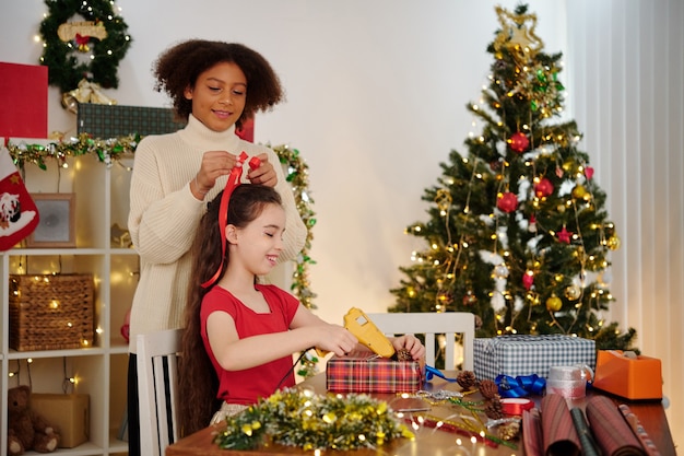 Smiling teenage girl tying hair of her friend with red ribbon